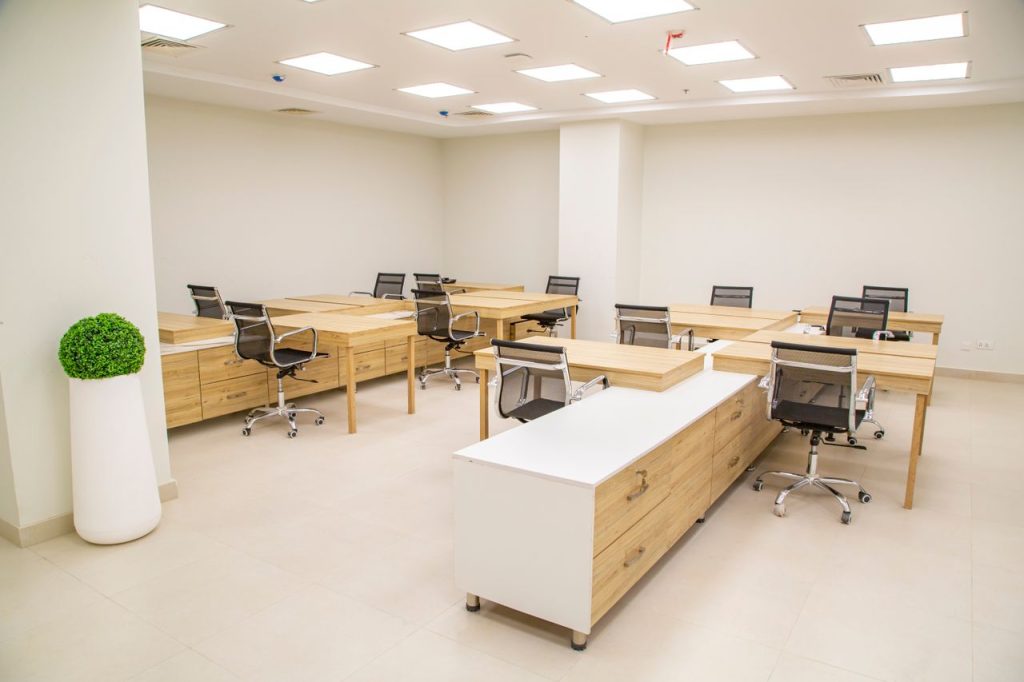 A bright, modern office space featuring wooden desks, rolling chairs, and ample lighting.